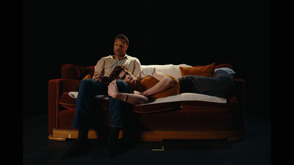 Trevor (played by Cliff Dunigan) sits on the couch with Misha's (played by Quinton Walker) head in his lap. The atmosphere is tense.