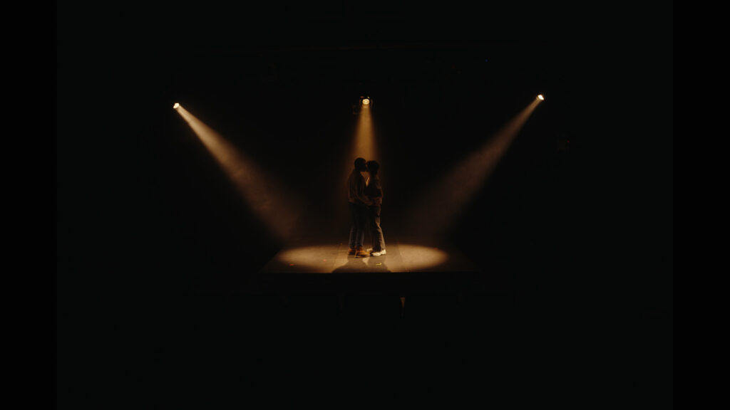 Misha and Trevor kiss under the stage lights.
