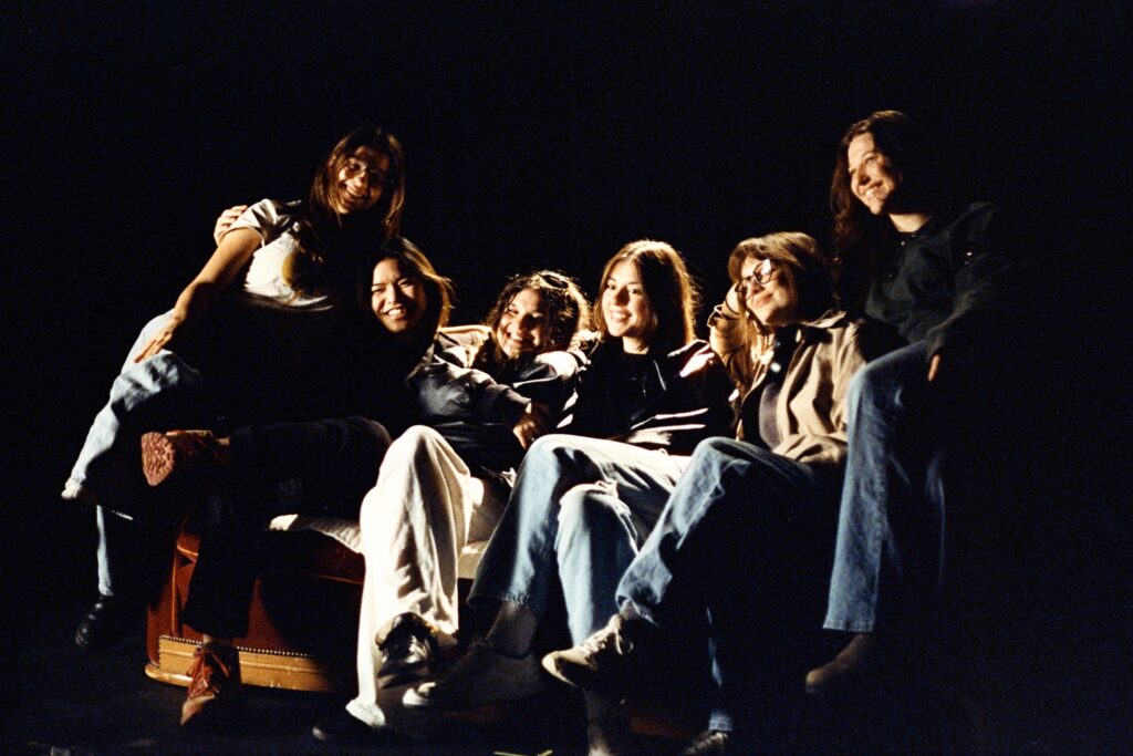 From right to left: Kayla (gaffer), Mary (key grip), Diana (intimacy liaison), Emily (first AD), Katie (production designer), and Sophie (best boy grip) smile for a picture on the couch