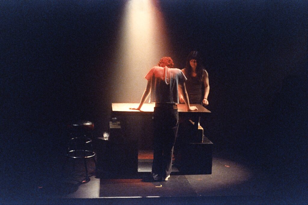 Quinton (playing Misha) and Gabriela (playing Reina) stand at a bar.