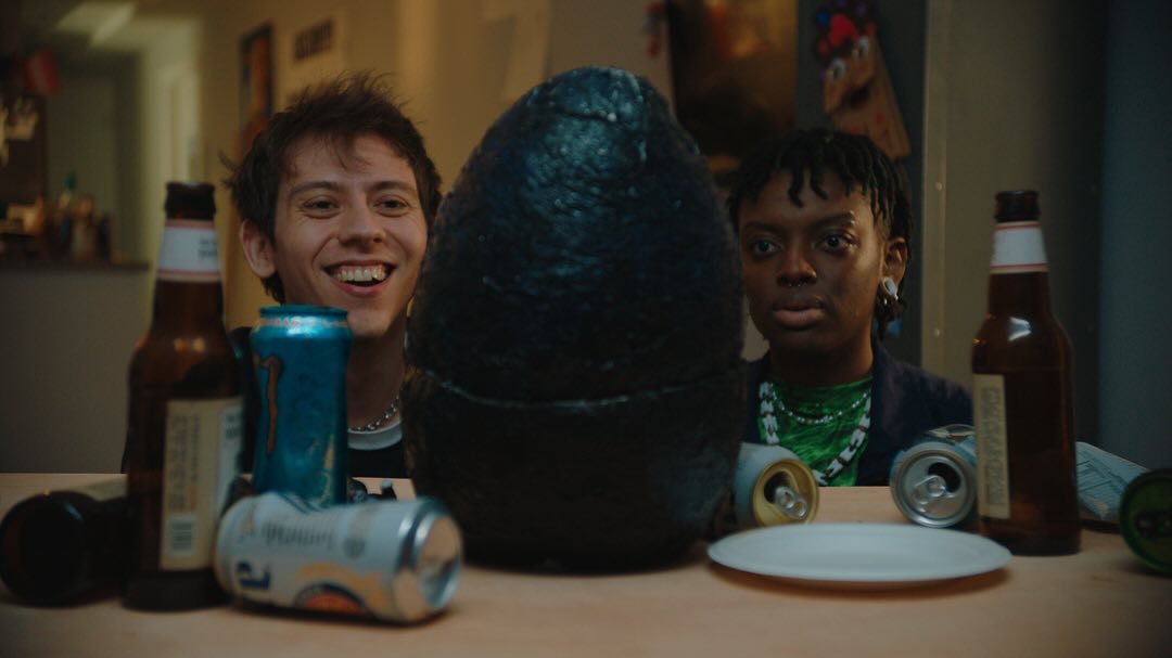 Worm Breath and Constance look at a large black egg, surrounded by beer bottles and Monster cans.