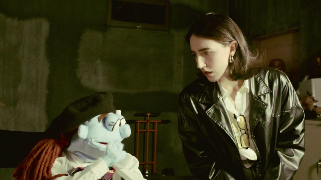 Phoebe (puppet, played by Frankie Temple Ruthless) and Graham (played by Zoe Gray Mazza) converse on a TV set.